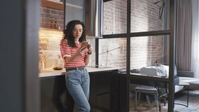 Adorable young woman drinking coffee or tea while holding cellphone. Pretty curly girl while chatting with someone at kitchen. Cherfuly smiling after getting positively message. Concept of rest. - Powered by Shutterstock - Get 15% off with code: PIKWIZARD15