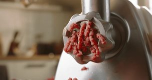 Meat coming through grinder plate. Closeup of minced meat flowing out of meat grinder. Slow motion blurred background kitchen. Advertising. Preparation of minced meat for hamburger by chef cook