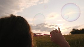 Back view of preteen girl blowing soap bubbles, having fun playing on field at sunset. Child plays with soap bubbles in nature. Happy childhood concept. Playful kid 7-8 years enjoy summer. Slow motion - Powered by Shutterstock - Get 15% off with code: PIKWIZARD15