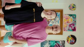 Young gen Z couple with shaved heads standing together in the living room, embracing, posing together on camera with a smile. Vertical clip, video portrait