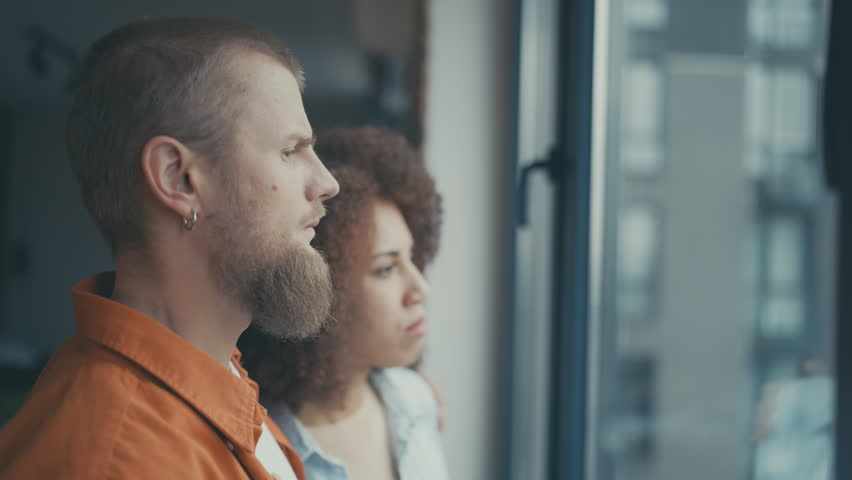 Sad interracial couple feeling worried about future while looking out the window Royalty-Free Stock Footage #1105802717