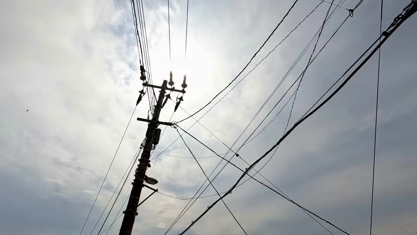 Broken electricity wires blowing in wind with bright sun in background