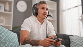 Young hispanic man playing video game sitting on sofa looking upset at home