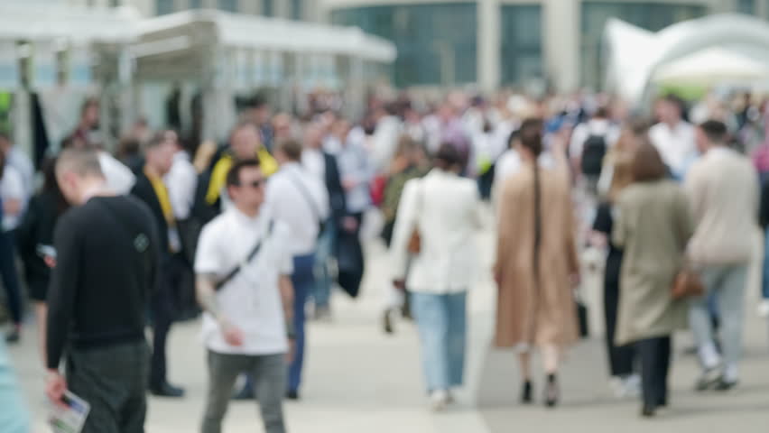 Defocused real time of many people walking on city street near building while going to festival during weekend