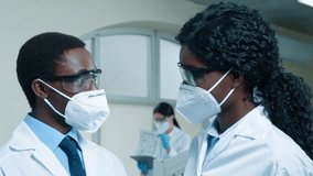 African American scientists working at laboratory room. Multiethnic woman and man dressed up in safety glasses and medical masks. Senior female scientist explain task to colleague. - Powered by Shutterstock - Get 15% off with code: PIKWIZARD15
