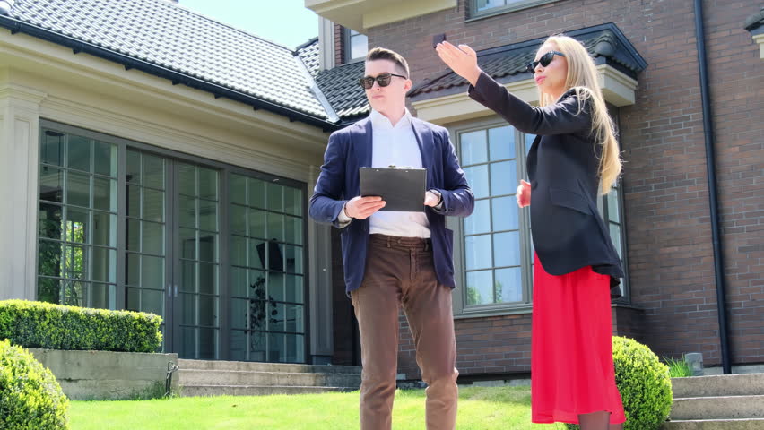 Property manager with clipboard shows summer residence to blonde client. Potential buyer points at cottage yard lit by sunlight Royalty-Free Stock Footage #1105814391
