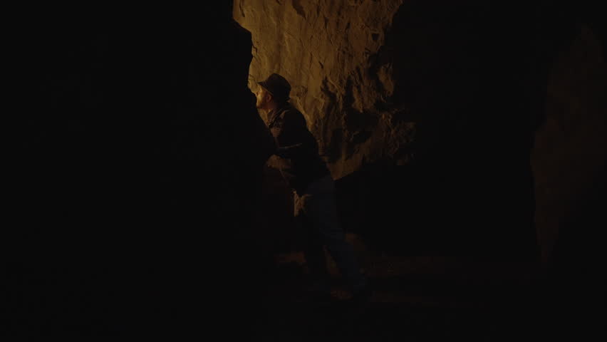 Male Adventurer Exploring Stone Rock Cave in Darkness Outside Using Torch Light