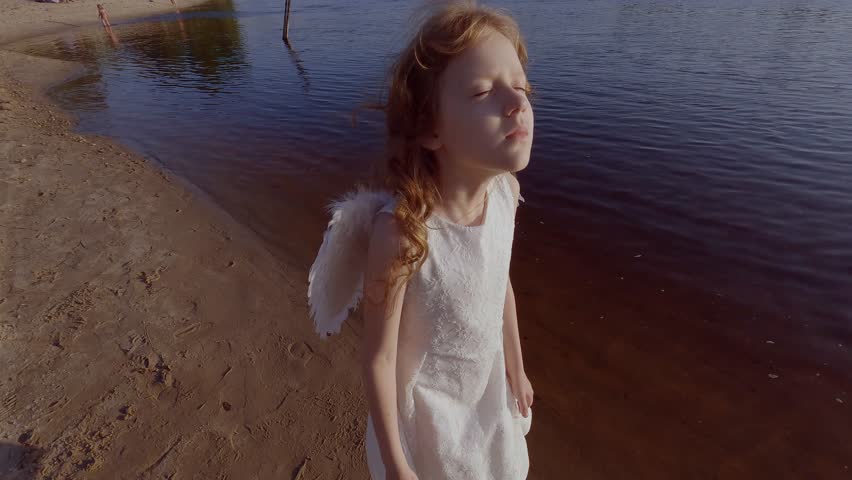 Cute little angel girl with wings near the water and is romantically bored.