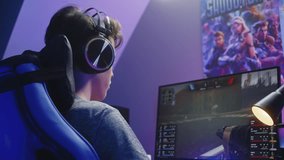 Young gamer in headphones plays in first person shooter on computer and loses round in PvP multiplayer game. Online video game live streaming or esports competition. Gaming at home concept. Back view.