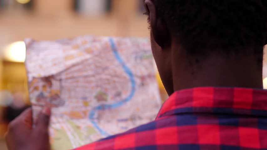 Back view of young african man trying to orient himself by looking at the map of the city | Shutterstock HD Video #1105826871