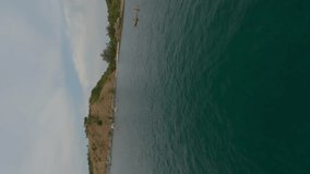 Vertical video. Aerial view island tropical sea mountain tourists floating canoe yacht sunset cloudy sky. FPV sport drone low shot active people holiday natural resort water transport lagoon scenery