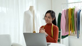 Woman designer entrepreneur showing clothes product on live online social media streaming and packing into cardboard box to preparing for shipping customer delivery at home