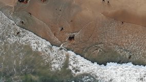 High quality 4K aerial video of a sea shore, with waves hitting on the beach. Taken with a drone flying over the beach.