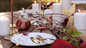 Table setting with white plates, gold cutlery, maple leaves, pumpkins, burning candles on wooden table outdoors. Stylish autumn decorated picnic in the park for Thanksgiving day, wedding, Halloween - Powered by Shutterstock - Get 15% off with code: PIKWIZARD15