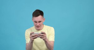Concentrated caucasian man losing video game by phone on blue background