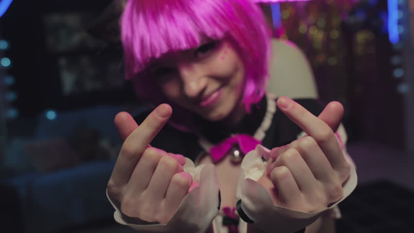 Selective focus shot of modern gen Z girl wearing cosplay outfit with pink wig and cat ears showing mini hearts gesture Royalty-Free Stock Footage #1105840765