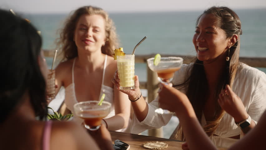   women cheering and clinking glasses with cocktails in sea view rooftop cafe. Multiethnic female friends drink beverages have fun at cocktail party in a tropical outdoor. 3D Illustration Royalty-Free Stock Footage #1105842943