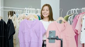 Young asian woman business owner at fashion store using smartphone live streaming for sale fashion clothing to customer and present detail on social media, Online shopping concept.