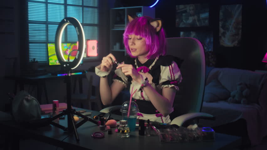 Handheld shot of young gen Z woman wearing cosplay outfit with pink wig and cat ears doing make-up while recording video for blog on smartphone Royalty-Free Stock Footage #1105844987