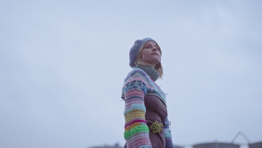 A low-angle arc shot of a woman wearing colorful knitwear, looking around during daytime