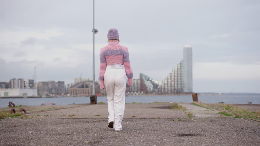 A woman wearing a cozy pink and purple wool sweater walks away from the camera