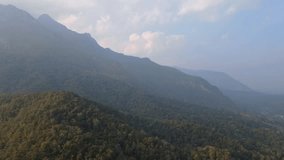 High-angle video from a drone, seeing the top of Doi Luang Chiang Dao, a huge mountain, lush green forest, bright fog in the morning, low light, before morning, the sun shines beautifully.