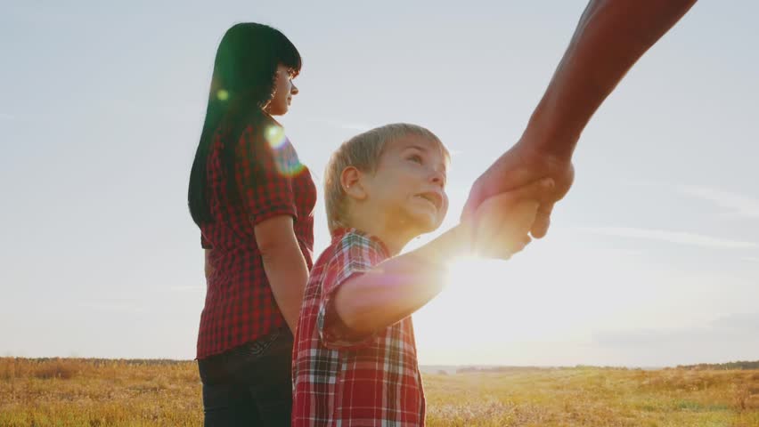 son in the park. happy family go hand in hand with son in sun nature in park at sunset silhouette. happy family a kid dream concept. little boy outdoors holding father hand and mother looking up Royalty-Free Stock Footage #1105853257
