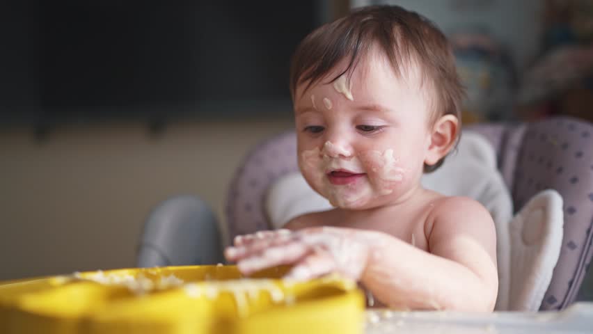 baby eats dirty. happy family kid toddler concept. baby girl dirty sitting messing with food at the table for feeding in the kitchen. grimy toddler lifestyle in the kitchen