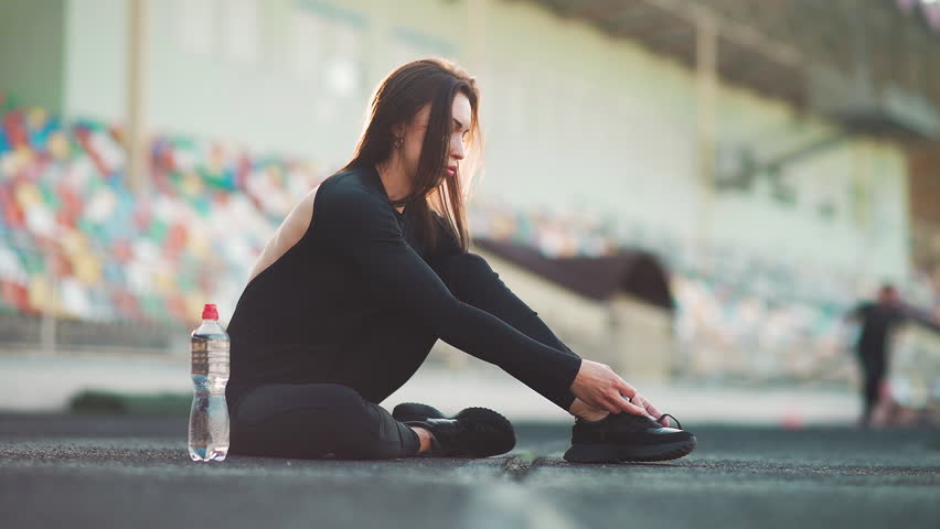 A cute runner girl is preparing for a race. The athlete girl is tying the laces on the sneakers. Sport and healthy lifestyle concept.