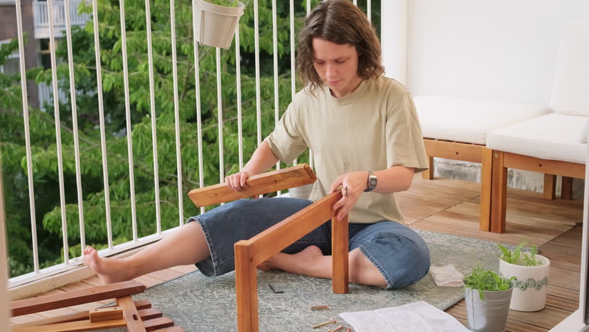 Confused  young curly woman trying to assemble garden furniture on her balcony on her own. Royalty-Free Stock Footage #1105856741