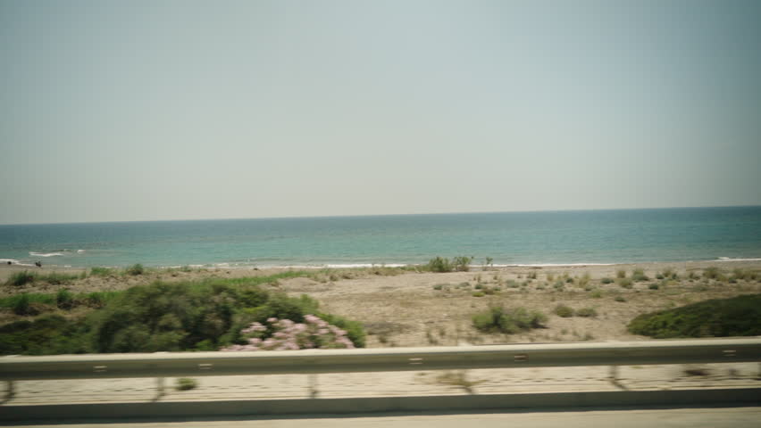 The view from the window of a car driving along the sea and beaches with pink flowers and shrubs, in slow motion.