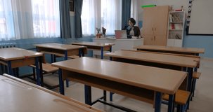 Camera moving towards beautiful female teacher sitting in classroom with empty desk. Portrait view. Educational background video in 4k resolution with copy space. Back to school concept.