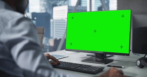 Over the Shoulder Footage of a Close Up Computer Screen with Green Mock Up Template. Anonymous Man Working in Office, Browsing Internet and Researching Business ata Online Stock-video