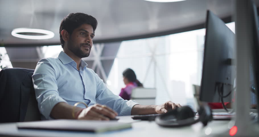 Portrait of a South Asian Financial Securities Trader Working on Desktop Computer in a Modern Office. Handsome Indian Accountant Bookkeeping Financial Affairs of a Business Venture Royalty-Free Stock Footage #1105861243