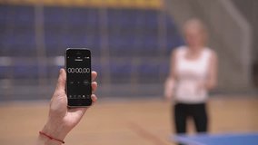 holding a stopwatch.table tennis. a woman trains using a racket and a table tennis ball. stopwatch on smartphone.High quality Full HD video recording