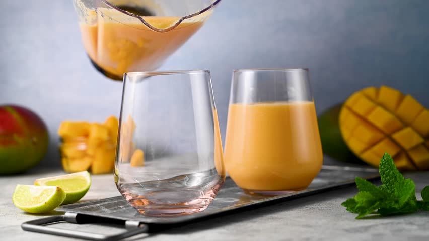 Pouring mango smoothie in a glass with fresh mango, mint and lime.