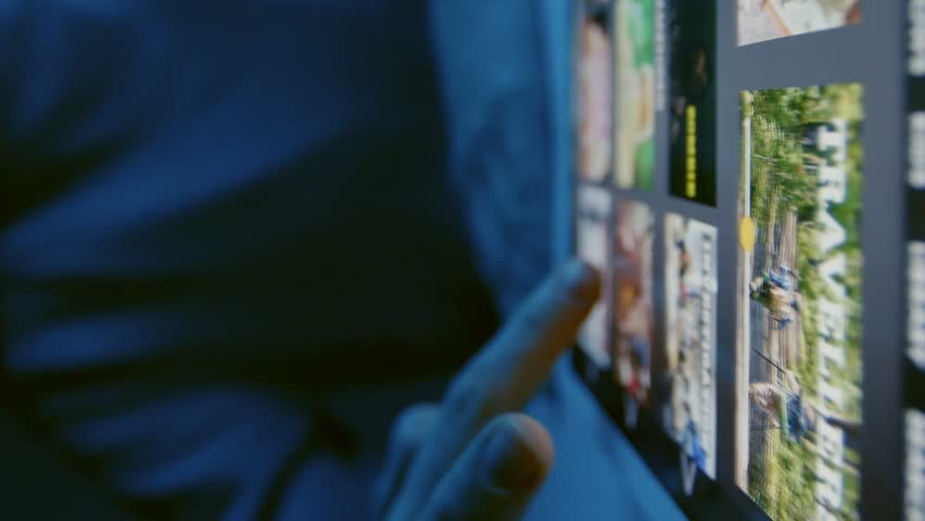 Close up of unrecognizable woman sitting at table with tablet lying down, choosing film to watch on stream service indoor at night time