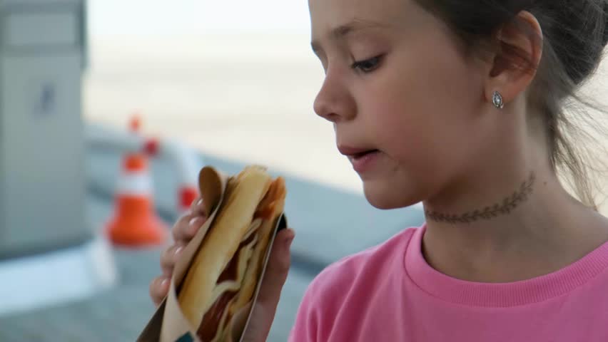 A young girl appetizingly eats a hot dog at a gas station. Rest while traveling. Close-up. Royalty-Free Stock Footage #1105863723