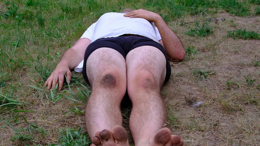 Barefoot obese man wearing white shirt and only briefs lying on the ground in his back yard after pool party.