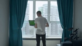 The screen in the laptop is green. Media. A man picking at a laptop with a green screen in front of a light window.