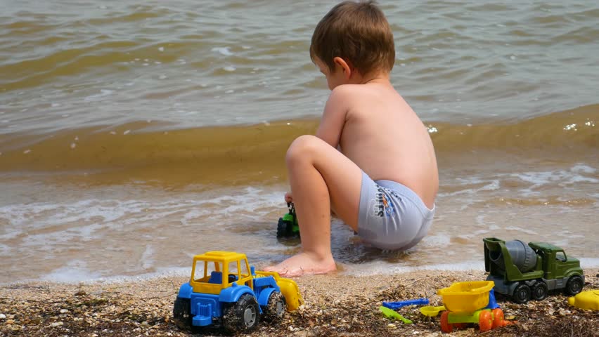 A small child, a boy playing with toys in the sand on the seashore. Royalty-Free Stock Footage #1105876259
