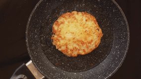 A wooden spatula turns over a fried potato pancake with a crust fried in boiling oil in a pan. High quality FullHD footage