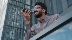 Happy smiling Indian man businessman business employer guy record voice message on phone audio chat dictate voicemail in microphone using AI mobile assistance speak smartphone talk loudspeaker in city - Powered by Shutterstock - Get 15% off with code: PIKWIZARD15