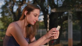 A beautiful woman sits in the park, sending some messages to her friends and family using her phone.
