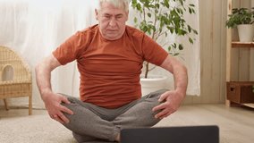 Happy mature senior man doing exercises of gymnastics at home online with laptop. Healthy lifestyle, fitness, recreation, well being. Elderly male exercising training, stretching. Old man working out.