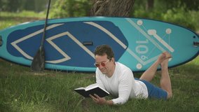 a man reads a book in the park, lying on the grass. man and sap board.slow motion video. High quality Full HD video recording