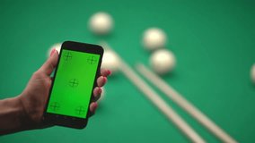 a woman holds a smartphone in her hand with a green screen. game of billiards. slow motion video. close-up.High-quality FullHD video recording