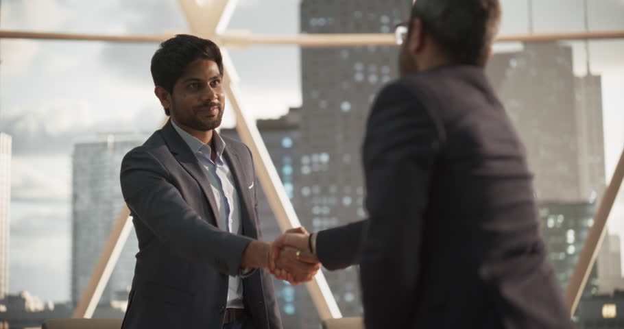 Young Indian Businesspeople Closing a Business Deal at a Meeting Room in Corporate Modern Office. Two Men in Classic Suits Shake Hands and Celebrate Successful Partnership