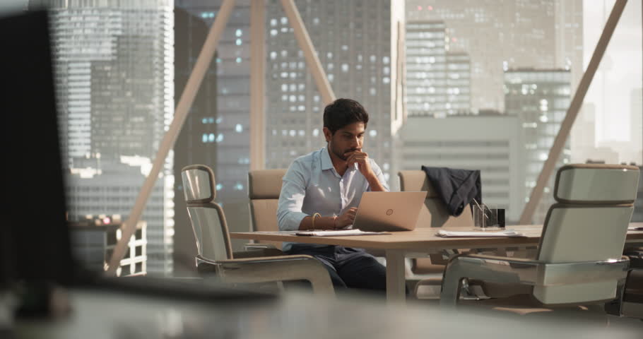Portrait of a Young Indian Account Manager Working on a Laptop Computer in a Modern Corporate Office. Businessman Dealing with Financial Reports, Preparing a Growth Plan for the Company