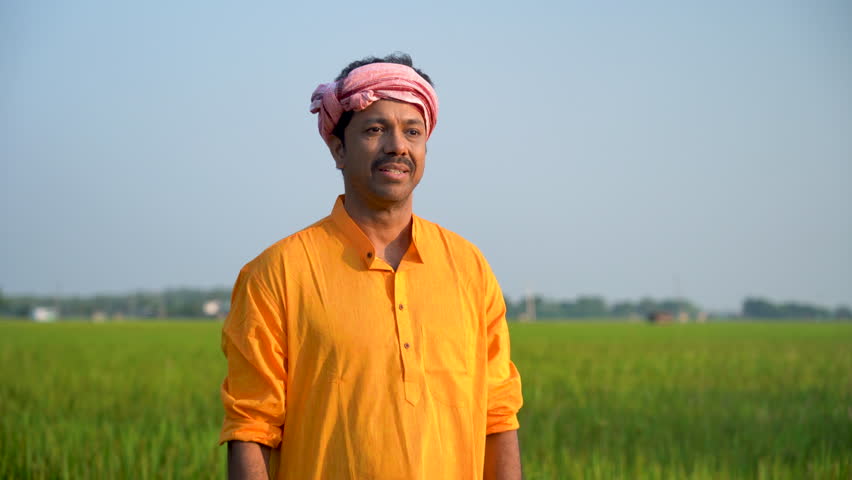 A happy Indian farmer during harvest time, standing proudly in his field, a smile adorning his face. The fruits of his labor bring joy as he witnesses the bountiful rewards of hard work in 4k footage. Royalty-Free Stock Footage #1105891971